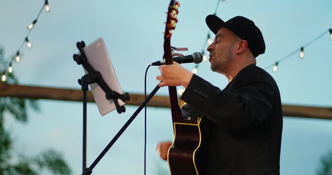 Male Acoustic Guitarist Singing Under String Lights at Outdoor Evening Performance