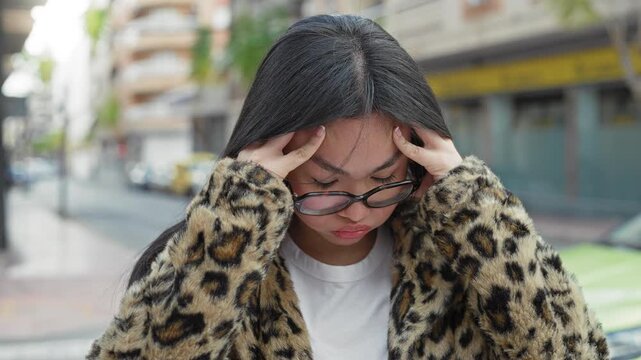 Woman with glasses holding her temples for headache, hands to head on a city street wearing leopard coat; stress, focus.