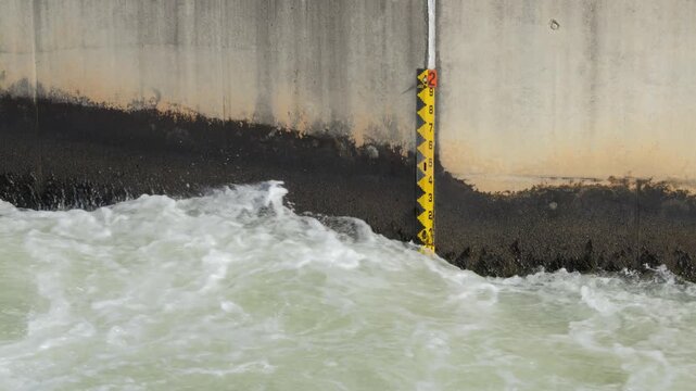 Yellow and black depth gauge against concrete wall with strong flowing water rushing past