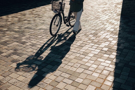 Person walking with bicycle casting long shadow on pavement