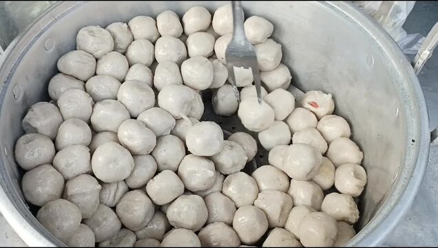 Fresh steamed fish balls in a large metal steamer tray, traditional street food preparation with a hand using a fork to serve ready-to-eat fish balls