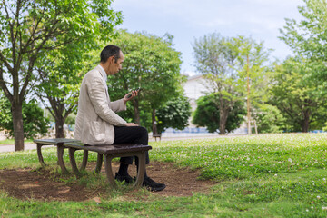 Fototapeta premium 公園のベンチでスマートフォンを見る日本人男性
