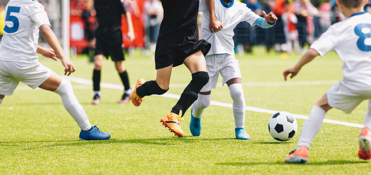 Youth Soccer Match Action: Kids Dribbling and Defending Ball on Green Pitch. Kids Soccer Tournament Banner: Cropped Action View of Legs and Ball on Field
