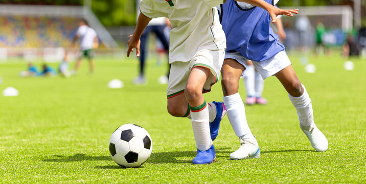 Kids Football Dribbling Drill: Close-Up of Young Player Controlling Ball During Match. Action View of Junior Players in White and Blue Uniforms
