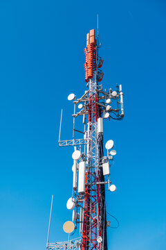 Cellular communication tower with multiple antennas and microwave dishes against clear blue sky, modern telecommunications infrastructure