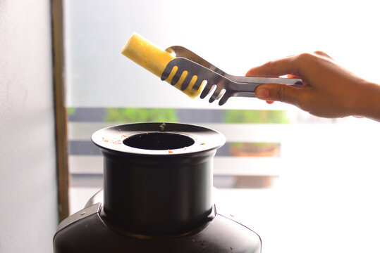 a hand using a tong to pick up a piece of fresh pineapple into the fruit juice extractor in order to make a fresh juice at home