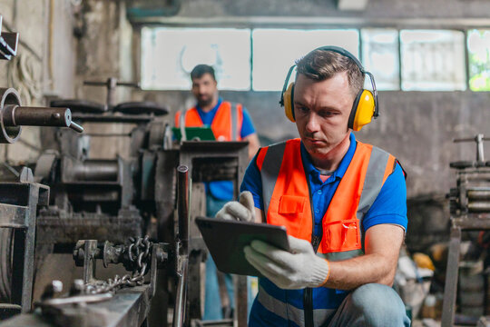 Factory Technicians Reviewing Machine Maintenance Checklist in Metal Workshop