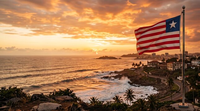 Liberian flag waving over Monrovia coastal city landscape during golden hour sunset with ocean waves