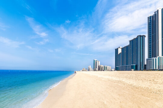 Sandy beach and modern skyscrapers on coastline of Ajman, UAE. Beautiful turquoise sea and skyline. Summer vacation and tropical resort concept.