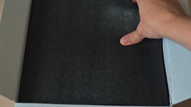 Hands unpack items from black foam inside a box. The process takes place at a table, focusing on the careful removal of packaging materials