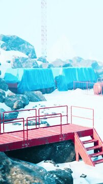 A red platform stands in a snowy area with rocks. Blue tarps cover some equipment. Snow is all around, and the scene is bright and cold, showing winter conditions.