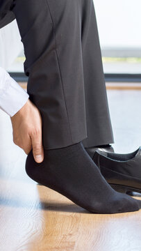 Tired businessman with joint ache touching her ankle sitting on a couch