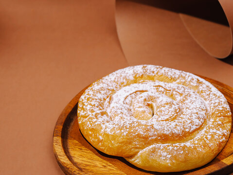 Traditional sweet ensaimada pastry dusted with icing sugar. Delicious spiral bun dessert served on wooden plate.