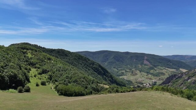 Montagne verdi e boschi che si estendono verso una valle con un piccolo insediamento, sotto un cielo limpido