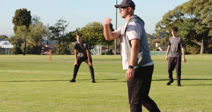 Coach throwing ball on cricket field in drill while teen fielders tracking, catching, copy space