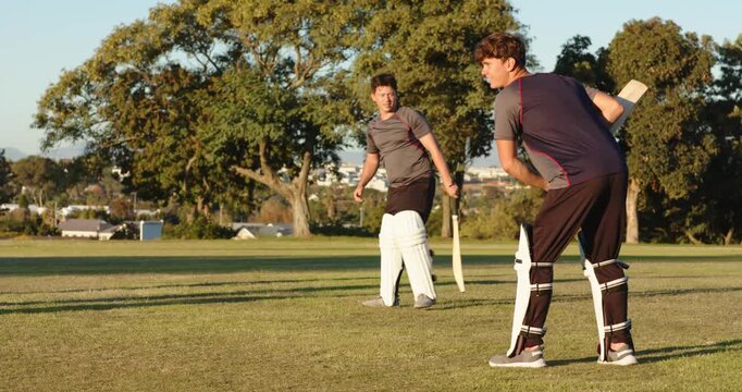 Male coach clapping, encouraging batsmen tapping red ball, bats on cricket field, copy space