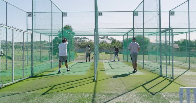 Practicing diverse male teammates bowling and batting in outdoor cricket nets with bats, wickets