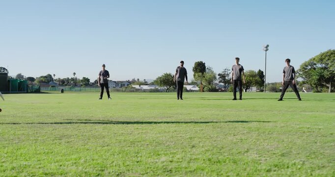 Diverse teams practicing cricket drill on grass field, bat tapping shots, intercepting ball