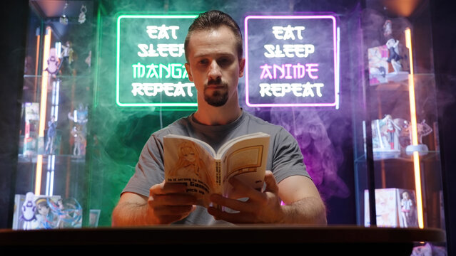 Man reading manga comic in cyberspace room with neon signs and merch showcases