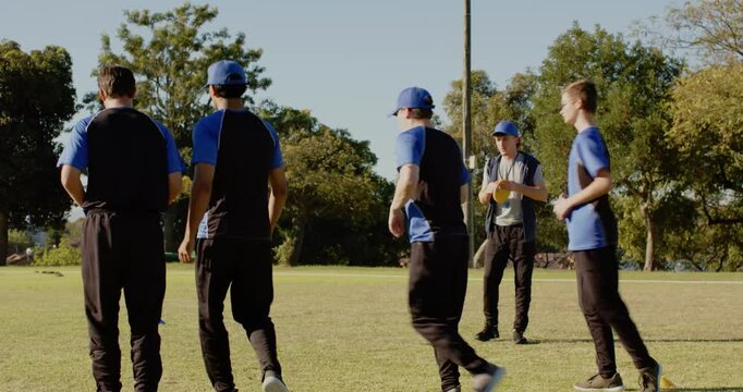 Jogging diverse male teammates warming up on grass field in park, with yellow disc, cone