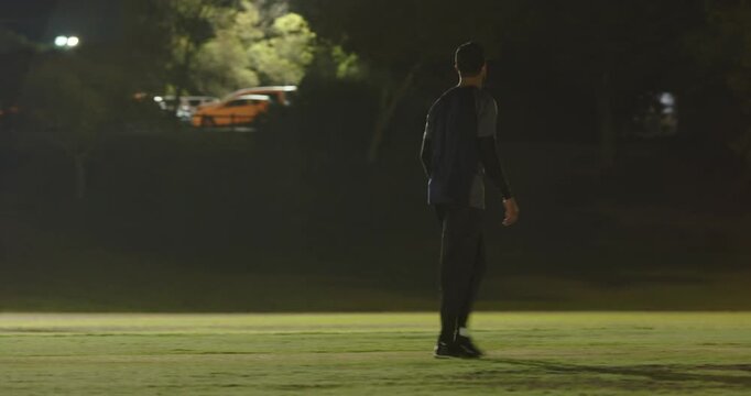 Batsman with bat jogging between stumps after bowler's run up taking guard under floodlights