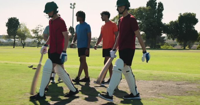 Grey-shirted boy fielder directing team at park, blue-shirt bowler running up delivering ball