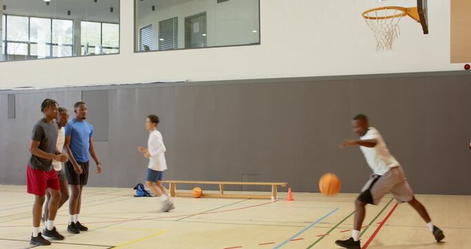 Receiving pass asian player dunking ball in gym while diverse male friends practicing scoring moves