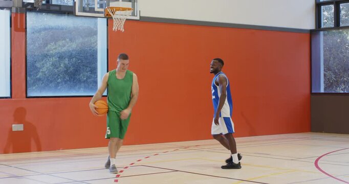 Driving past opponent, male players shooting basketball at gym hoop, rebounding, and handshaking