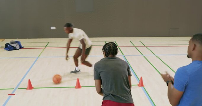 Receiving basketball, african american youth dribbling through orange cones in the hardwood