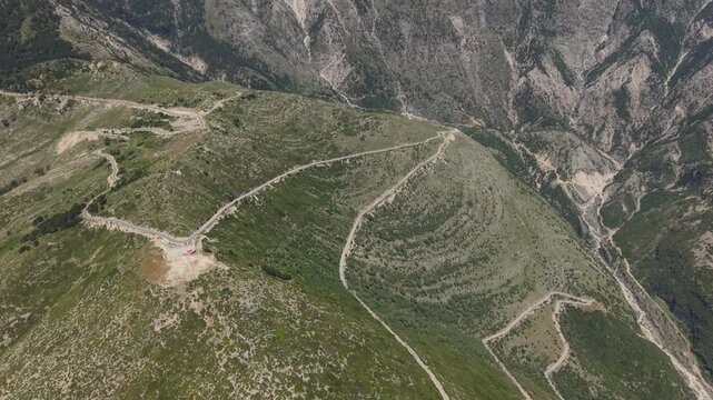 Aerial view of a winding mountain road on green slopes and rocky terrain in Himare, Vlore County, Albania.