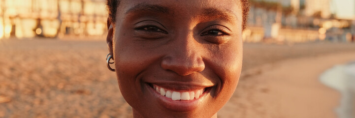 Fototapeta premium Portrait of an attractive girl on the beach at sunrise, looking into the camera and smiling. Panoramic. Panoramic