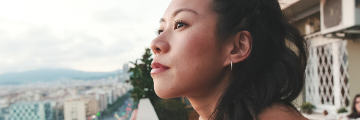 Obraz premium Close up, young woman standing on the balcony looking at the city at sunset. Panoramic