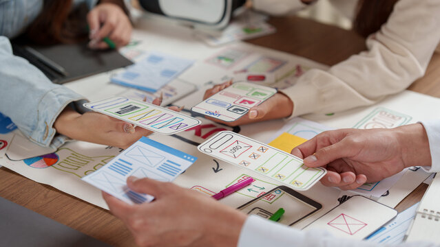 Cropped hands of designers comparing mobile app paper wireframes for UX UI prototyping