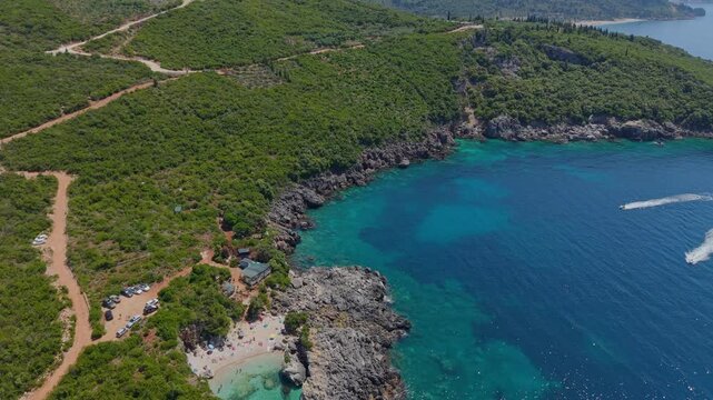 Aerial view of Aquarium Beach featuring turquoise waters, rocky cliffs, and lush green hills along the coastline in Jala, Vlore County, Albania.