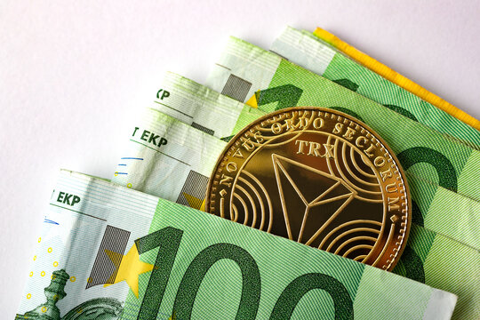  Criptomonedas y tecnolog&iacute;a.Monedas de oro TRX Tron con billetes de euro sobre fondo blanco, imagen de primer plano.