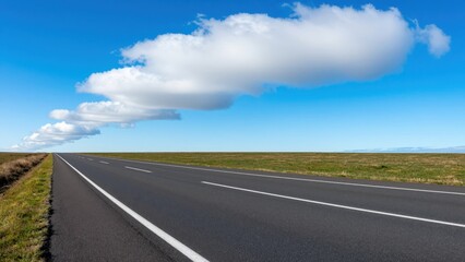 Fototapeta premium Open Road Ahead: An empty asphalt road stretches towards the horizon under a vast blue sky with a trail of fluffy white clouds, symbolizing a journey of endless possibilities and freedom.