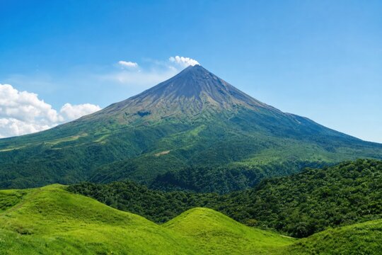 Active stratovolcano emitting light steam from peak, surrounded by lush green tropical forest hills under clear blue sky, peaceful and serene wide angle landscape