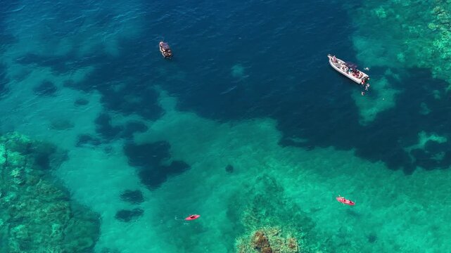 Aerial view of boats and red kayaks floating on the crystal clear turquoise water of Aquarium Beach with visible rocky seabed near Jala, Vlore County, Albania.