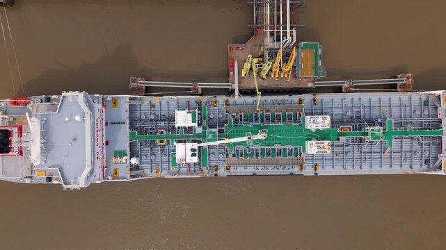 Aerial view of a large industrial tanker ship docked at a terminal with yellow loading arms and pipes on the river Thames in Dartford, England, United Kingdom.