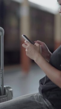 Close-up of traveler using smartphone beside luggage, ideal for travel app, mobile ticket, online booking, trip planning, transportation and journey concepts