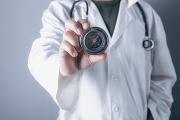 Male doctor holding a compass in his hand on a gray background. © Artvibe