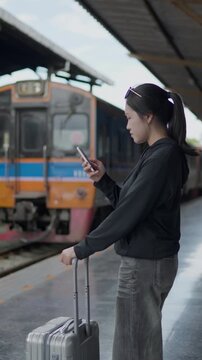 Traveler using a smartphone on a train platform with luggage, ideal for travel app, mobile ticket, train arrival, rail travel, tourism and journey concepts