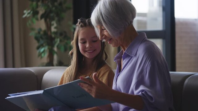 Senior woman showing family photos to her granddaughter, remembering the past