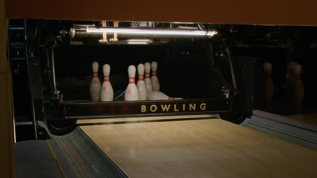 Bowling ball rolling down lane and hitting pins, followed by automatic pinsetter machine clearing and resetting remaining pins. Footage suits sports marketing and leisure industry promotions