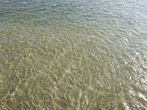 Crystal clear ocean water surface with sun reflection on sand bottom