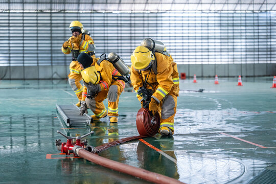 Professional firefighters wearing yellow protective suits practicing fire hose management during emergency response training inside a building