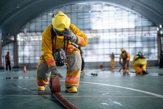 Professional firefighters wearing yellow protective suits practicing fire hose management during emergency response training inside a building