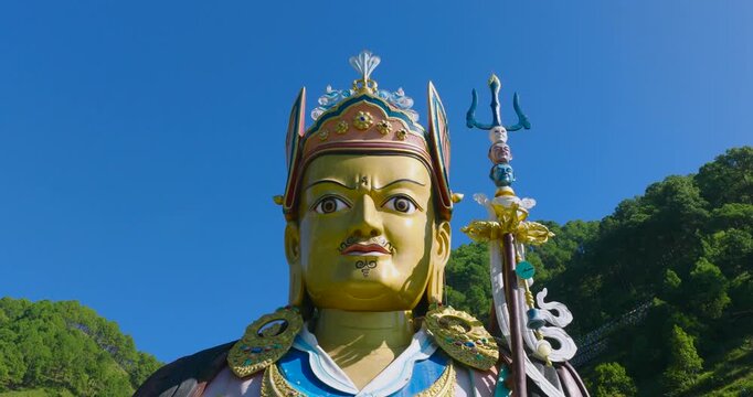 Aerial pull out shot reveals a vibrant blue Guru Rinpoche statue in Pharping, Nepal, contrasting sharply against the lush green hills in the backside