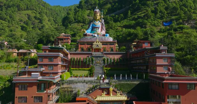 Aerial push-in shot at Dollu Monastery in Pharping, Nepal, moving from the courtyard steps up to the giant Guru Rinpoche statue, contrasting green hills in the backside.