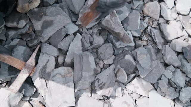 Top-down view: a gloved hand grabs a slab of Jurassic shale and starts hammering the chisel in. Overhead perspective on the focused search for fossils in Holzmaden, Germany &ndash; discovery awaits.